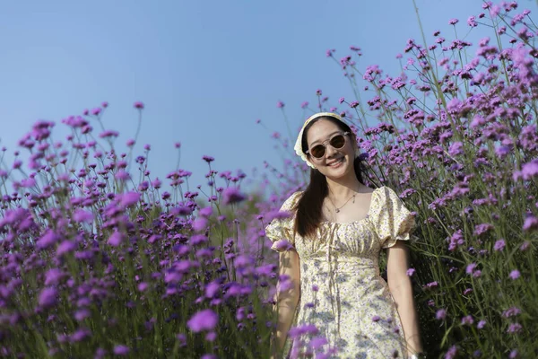 Güzel mor çiçek tarlasında gülümseyen mutlu genç Asyalı kadın. Açık mavi gökyüzü ile yaz tatilinin tadını çıkaran kişinin yaşam tarzı portresi