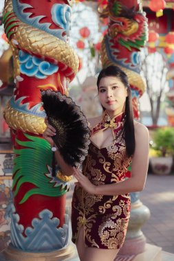 Geleneksel Çin peynirinde güzel bir Asyalı kadın elinde yelpaze, kültürel kutlama sırasında ejderha sütununun yanında duruyor, kendinden emin bakışlarıyla