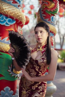 Geleneksel Asyalı ya da Cheongsam elbiseli zarif Çinli kadın tapınakta ejderha sütunun yanında yelpaze tutuyor, kültürün ve mirasın güzel ifadesi.