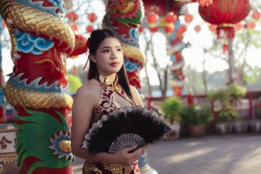 Geleneksel kırmızı Cheongsam yelpazeli zarif Çinli kadın sakin bir ifadeye sahip. Tapınaktaki güzel pozu zengin kültürü ve kutlamaları yakalıyor.