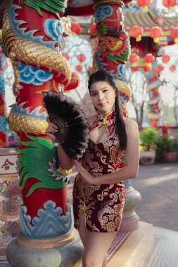 Kırmızı Cheongsam elbiseli, kendine güvenen Asyalı kadın Çin tapınağında poz veriyor. Ejderha sütunları ve fenerlerle kutlamalardaki huzurlu ifadesi şenlikli hissettiriyor.