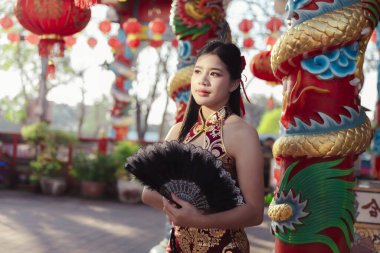 Geleneksel Çin elbiseli güzel Asyalı kadın tapınakta yelpaze tutuyor. Kutlama sırasında yüzü kırmızı fenerlerin arasında huzurlu ve zarifti.