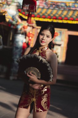 Kırmızı geleneksel Çin elbisesi giymiş kendine güvenen Asyalı kadın festivali kutluyor. Güzel bir açık hava portresi canlı bir kültür ve mutlu bir gülümseme.