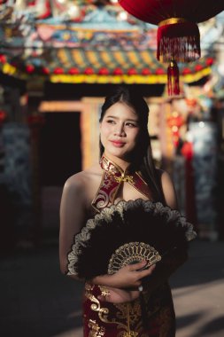 Geleneksel kırmızı Çin elbisesi içindeki mutlu, güzel Asyalı kadın yeni yıl kutlamaları sırasında siyah yelpaze tutuyor. Canlı Çin Mahallesi 'nde dingin görünümlü bir festivalden hoşlanıyor.