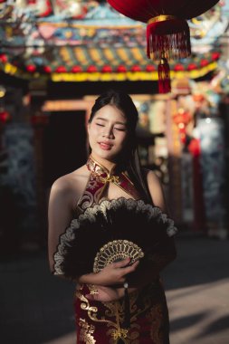 Geleneksel Çinli kırmızı elbiseli mutlu Asyalı kadın kutlama sırasında yelpaze tutuyor. Arka planda şenlikli kırmızı fener olan kişinin huzurlu portresi