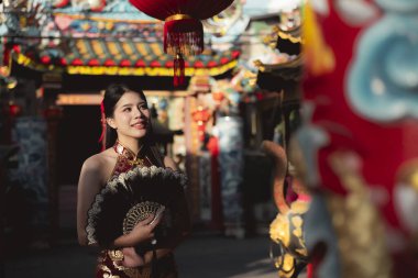 Geleneksel Çinli elbiseli mutlu genç Asyalı kadın Cheongsam, yeni yıl kutlaması sırasında canlı Çin Mahallesi 'nde kırmızı fener arka planında yelpaze tutuyor.