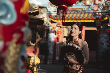 Geleneksel elbise giymiş, elinde yelpaze tutarken gülümseyen mutlu, genç Asyalı kadın. Güzel kız kültürel kutlamalardan ve dışarıda kırmızı fenerlerle eğleniyor.