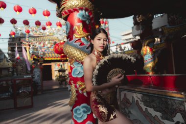 Kızıl Cheongsam 'lı özgüvenli Asyalı kadın, Çin Yeni Yıl Festivali' nde hayranını tutuyor. Ejderha ve kırmızı fener süslemeleri ile kültürün ve geleneğin kutlanması