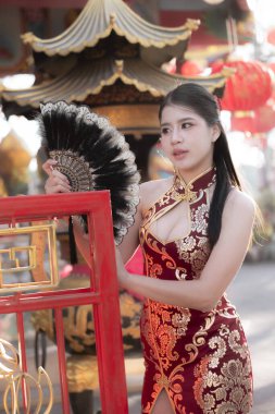Geleneksel kırmızı Çin elbisesi içinde güzel bir Asyalı kadın, festival sırasında yelpaze tutuyor. Onun sakin ifadesi zengin kültür ve geleneği yansıtıyor.