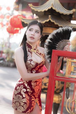 Geleneksel kırmızı Cheongsam 'lı zarif Asyalı kadın elinde siyah yelpaze tutuyor. Çin Yeni Yıl Festivali boyunca tapınaktaki güzel ve düşünceli bir ifade.
