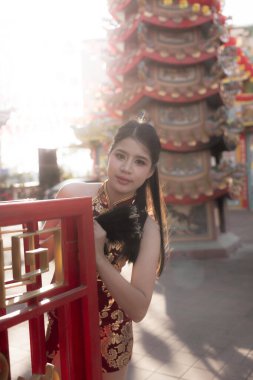 Geleneksel siyah ve altın rengi Cheongsam elbisesi giyen güzel bir Asyalı kadın. Serene Çinli kız güneşli festival sırasında Kızıl Tapınak tapınağında poz veriyor.