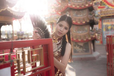 Geleneksel siyah Qipao elbiseli güzel Asyalı kadın Çin tapınağında yelpaze tutuyor. Düşünceli ve düşünceli bir ifade öğleden sonra güneşli