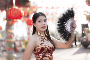 Çin kültürünün tapınaktaki kutlaması sırasında siyah yelpaze tutan geleneksel kırmızı Cheongsam giysili güzel Asyalı kadın.