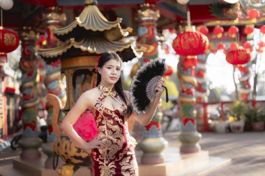 Çin kültürünü ve geleneğini kutlayan geleneksel kırmızı elbiseli kendinden emin genç Asyalı kadın. Güzel kırmızı fenerlerle dolu bir açık hava tapınağında canlı bir festival