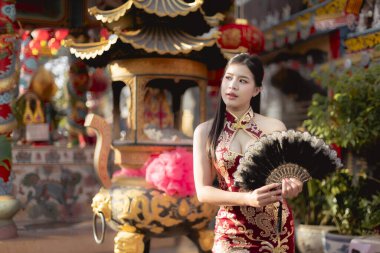 Serene Çinli kadın geleneksel kırmızı Qipao giyer ve elinde siyah yelpaze tutarak süslü bir tapınakta kültürel kutlama sırasında huzurlu bir anın tadını çıkarır.