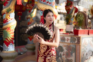 Geleneksel kırmızı Çin Qipao 'sunda Asyalı zarif bir kadın. Antik tapınaktaki dingin ifadesi kültürel kutlamalar sırasındaki sakin havasını yansıtıyor.