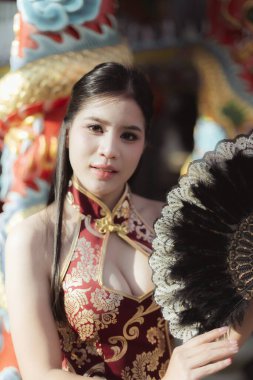 Geleneksel kırmızı Qipao elbiseli, kendine güvenen gülümseyen Asyalı kadın. Kültürel kutlama sırasında Çin tapınağındaki portrede siyah bir yelpaze vardı.