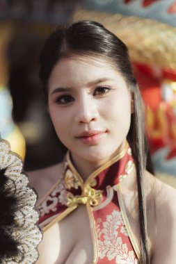 Geleneksel Çin Qipao elbisesi içinde güzel, sakin bir Asyalı kadın. Güzel bir portre. Kültür ve modanın zarafetini yansıtıyor. Açık havada kendine güvenen bakışlarla.