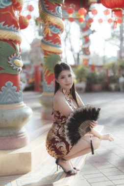 Geleneksel Cheongsam elbisesi giymiş zarif Asyalı kadın kültürel kutlama sırasında renkli Çin tapınağında zarif bir şekilde poz veriyor.