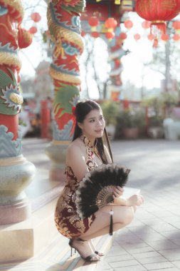 Geleneksel altın sarısı Qipao 'daki güzel Asyalı kadın, Çin' in yeni yıl kutlamaları sırasında tapınakta dingin bir gülümsemeyle hayranlarını kucaklıyor, kültürünü ve festivalini kucaklıyor.