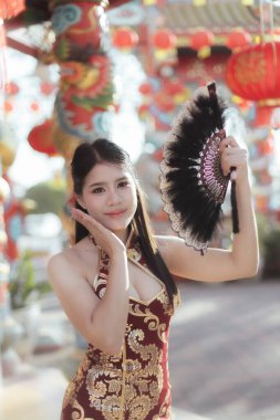 Geleneksel kırmızı Qipao elbisesi içindeki mutlu Asyalı kadın Çin 'in yeni yılını kutluyor. Bu güzel kadın portresi tapınakta yelpaze tutarken festival kültürünü gösteriyor.