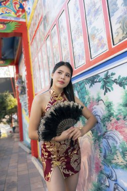 Kırmızı Qipao elbiseli güzel Asyalı kadın, Çin tapınağında kendine güvenen bir ifadeyle poz veriyor. Bu portre geleneksel kültür ve modayı yansıtıyor.