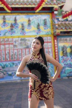 Geleneksel kırmızı Cheongsam elbisesi giymiş kendine güvenen Asyalı kadın Çin tapınağında poz veriyor. portre, seyahat ve turizm kültürü ve zarafetini somutlaştırıyor