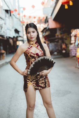 Çin Mahallesi 'nde sokakta kendine güvenen geleneksel Qipao elbiseli güzel bir Asyalı kadın. Festivalde kırmızı fenerle kültürel moda portresi