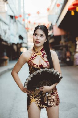 Kırmızı Qipao elbiseli kendine güvenen Asyalı kadın, Çin kutlamaları sırasında sokakta hayranlarını tutuyor. Düşünceli bir ifadeyle portre, geleneksel ve modern tarzın harmanlanması