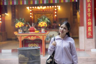 Geleneksel tapınakta düşünceli genç Asyalı kadın gezgin. İfadesi, duası sırasında derin bir tefekkür ve inanç gösteriyor, maneviyat ve kültürü vurguluyor.