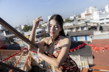 Şehrin çatısında geleneksel Çin elbisesi giymiş sakin, güzel bir Asyalı kadın. Qipao 'daki bu zarif bayan güneşli günün tadını çıkarıyor. Huzurlu ve mutlu.