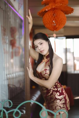 Geleneksel Çin cheongsam peynirli zarif ve güzel Asyalı kadın. İçerde şenlik fenerinin yanında poz verirken çok çekici bir ifadesi var.