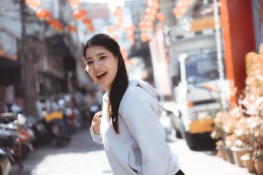 Canlı şehir caddesinde gülümseyen mutlu Asyalı kadın. Açık hava kentsel yaşam tarzının tadını çıkaran neşeli genç bir yetişkin. Kasabada yürüyen neşeli insan portresi