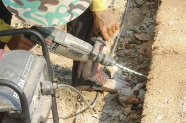 İnşaat işçisi ağır elektrikli aletle betonu delmeye odaklanmış. İnşaat alanındaki yıkım projesi için el emeği, sıkı çalışma ve sanayi