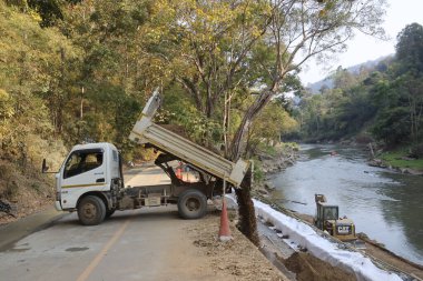 İnşaat alanındaki çöp kamyonu yol onarım projesi için toprağı boşaltıyor. Akan nehrin yanında altyapı iyileştirme ve erozyon kontrolü üzerine aktif çalışma
