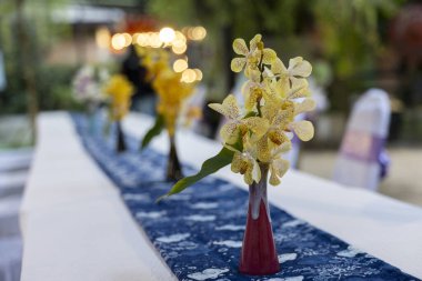 Uzun yemek masasında küçük kırmızı vazoda zarif sarı orkide çiçeği. Romantik düğün resepsiyonu için güzel masa dekorasyonu ya da huzurlu atmosferli bir ziyafet.