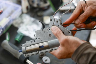 Odaklanmış kişi, hava yumuşak bir silah şanzımanı üzerinde teknik onarım ve bakım yapıyor. Hobi atölyesinde karmaşık silah mekanizması üzerinde çalışan el detayları