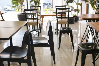 Modern siyah sandalyeleri ve ahşap masaları olan huzurlu ve boş bir kafe. Pencereden gelen doğal ışık müşterileri bekleyen sakin ve sessiz bir atmosfer yaratır.