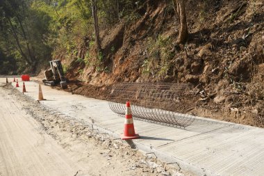 Dağ yamacında yol yapımı ve onarım işleri. Altyapı geliştirmek için çelik demirli yeni beton kaldırım. Turuncu güvenlik konisi tehlikeli iş alanı