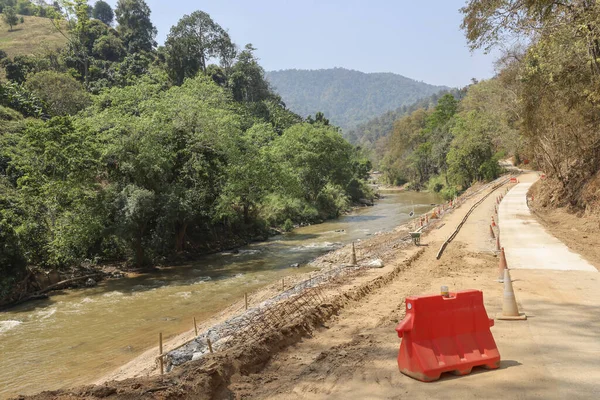 Kırsal dağ manzarasında akan nehrin yanında yeni beton yol inşaatı projesi. Bu sakin manzara uzak doğa alanındaki altyapı gelişimini gösteriyor