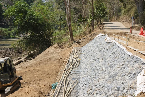 Rıhtım dengeleme ve aşınma kontrolü için yol kenarı inşaatı. Kamu güvenliği için bir mühendislik projesi sırasında çakıl tabakası yamaçta yer alır.