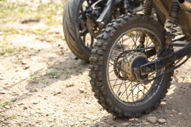 Kirli motosiklet tekerine yakın çekim. Toprak yolda topuzlu lastik var. Özel bisiklet off-road macerası ve açık hava seyahati için hazır, özgürlük hissi uyandırıyor.