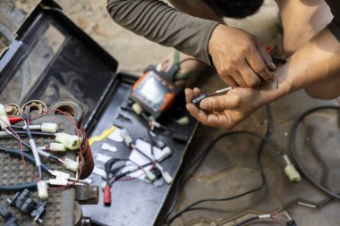 İşine odaklanmış tamirci, elektronik bir kabloda elle tamir işi yapan teknisyen. İşçi, scooter parçasının bağlantısını dikkatlice bir araçla düzeltir