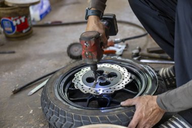 Motosiklet tekerleği tamiri ve fren diski bakımı yapan odaklanmış bir tamirci. Araç servisi işi için elektrikli araç kullanan profesyonel