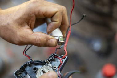 Odaklanmış mekanik el tamiri elektronik kablo ve alet ile dişli bileşeni. Elinde küçük bir parça tutan teknisyen, atölyede konsantrasyonu olan bozuk aletleri tamir ediyor.