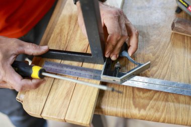 Odaklanmış marangoz elini marangozluk projesi için araç kullanarak kapat. Atölyedeki zanaatkar, ahşabı cetvel ve kare ile ölçüyor.