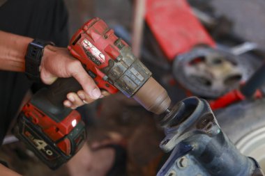 Atölyede kablosuz matkabı tamir için kullanan odaklanmış bir adam. Tamircinin eli, metal parçasında profesyonel bakım sırasında konsantrasyon gösteriyor.