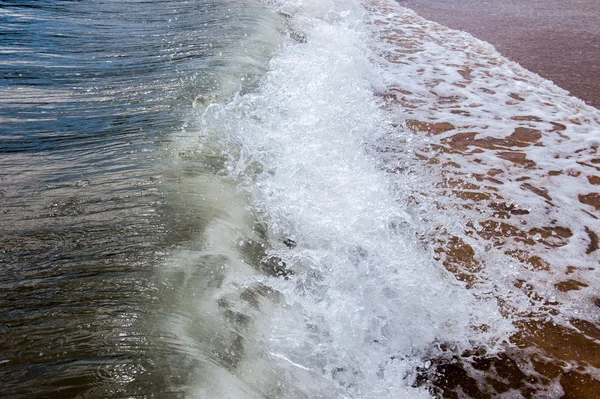 Golven als ze het zandstrand hit — Stockfoto