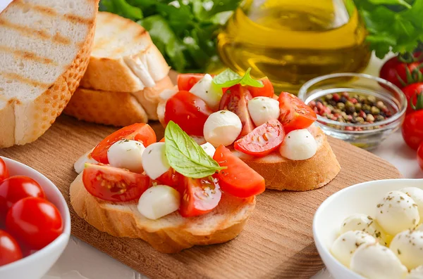 Bruschetta with cherry tomatoes and mozzarella on wooden board. — Stock Photo, Image