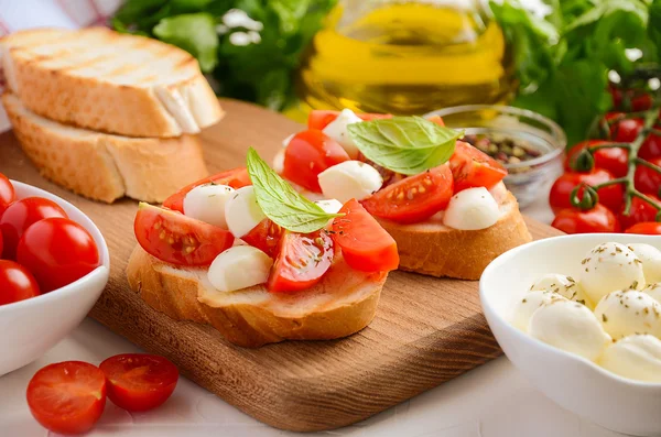 Bruschetta with cherry tomatoes and mozzarella on wooden board. — Stock Photo, Image